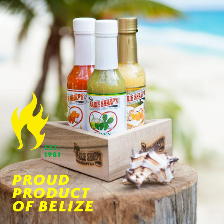 Drei Marie Sharp's Habanero Saucen im Holzständer an einem Strand in Belize