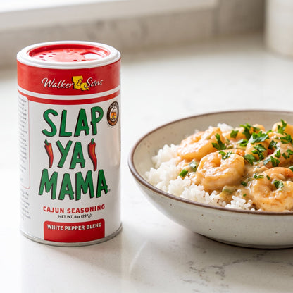 Slap Ya Mama White Pepper Blend Streuer neben einer Schale Shrimps in Rahmsauce mit Reis