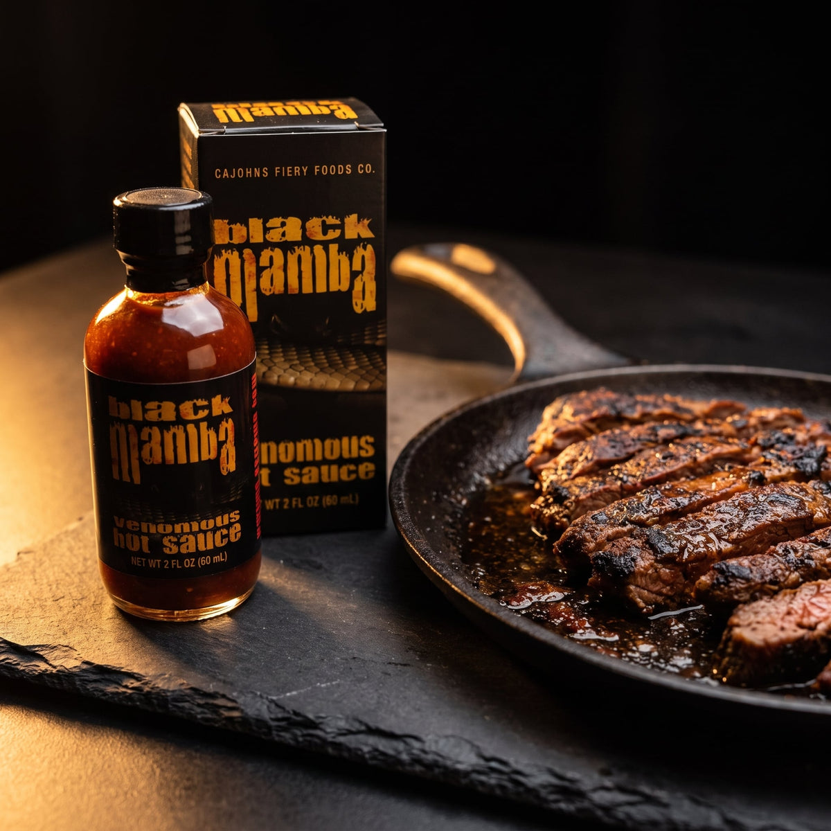 CaJohn's Black Mamba Hot Sauce mit Verpackung neben gegrillten Rindfleischstreifen in der Pfanne