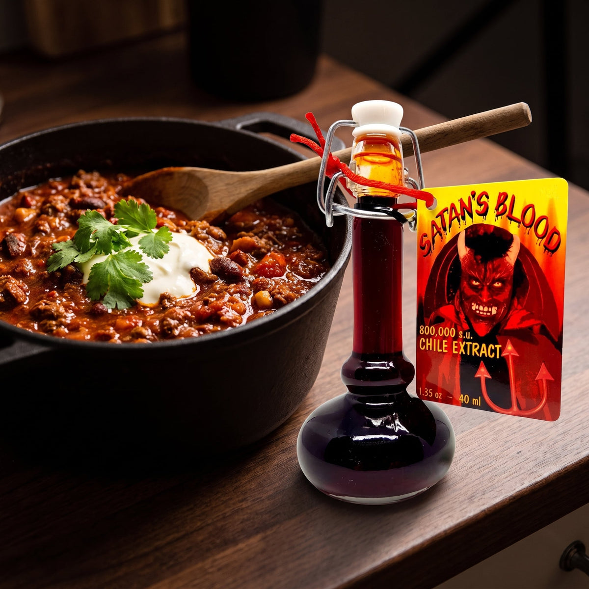 Satans Blood Chili-Extrakt neben einem Topf Chili con Carne mit Sauerrahm