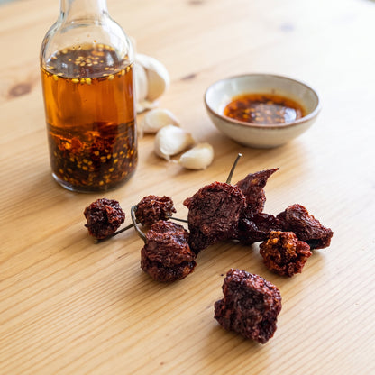 Getrocknete 7 Pot Brain Strain Chilischoten neben einer Flasche selbstgemachtem Chiliöl und Knoblauch