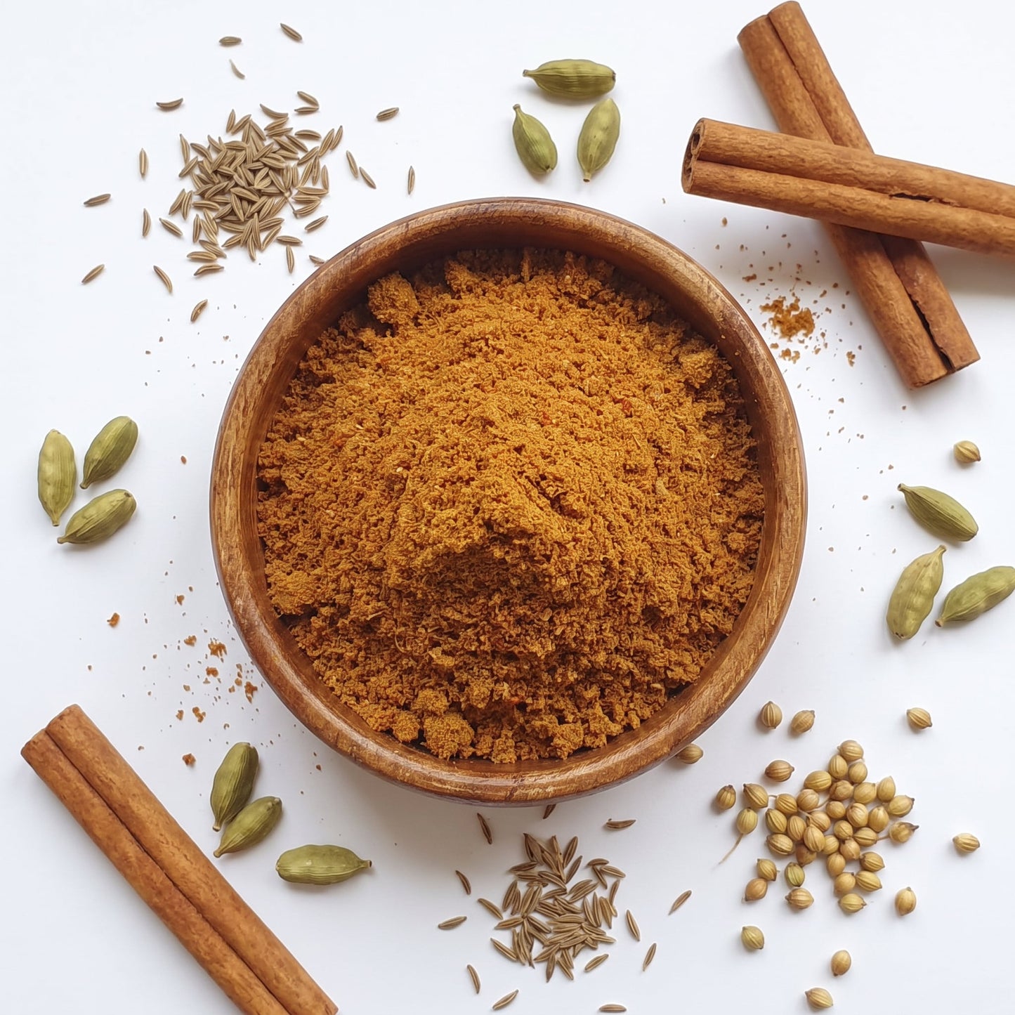 Madras Curry Powder in Holzschale, umgeben von ganzen Gewürzen