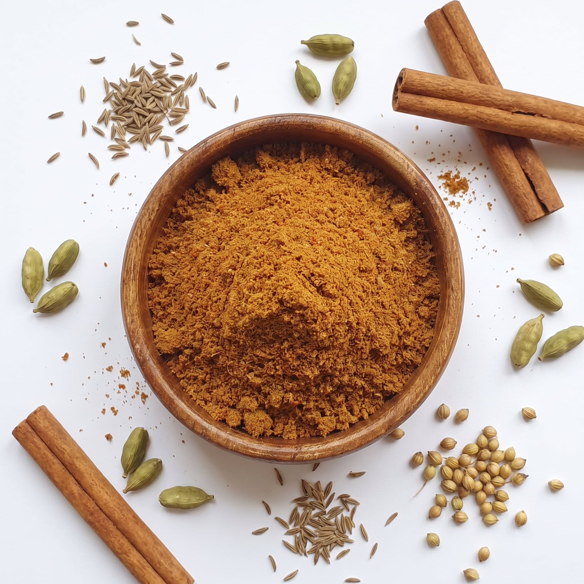 Madras Curry Powder in Holzschale, umgeben von ganzen Gewürzen