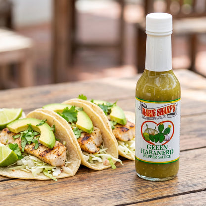 Marie Sharp's Green Nopal Habanero Sauce neben drei Fisch-Tacos mit Avocado und Koriander