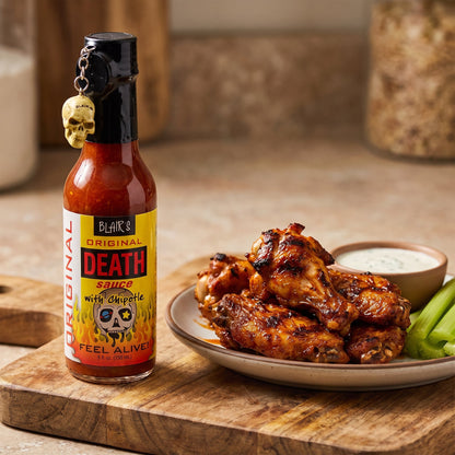 Blair's Original Death Hot Sauce neben gegrillten Chicken Wings mit Dip und Sellerie
