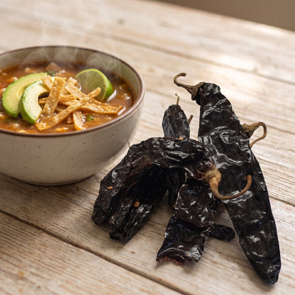 Getrocknete Pasilla Chilischoten neben einer Schale Tortillasuppe mit Avocado und Limette
