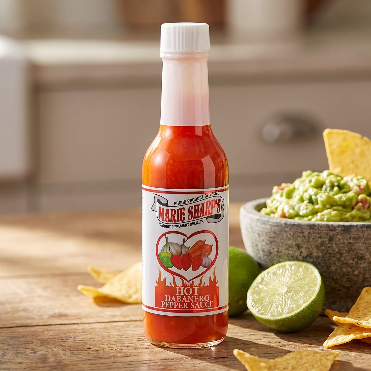 Marie Sharp's Hot Habanero Sauce auf einem Holztisch neben Guacamole, Limetten und Tortilla-Chips