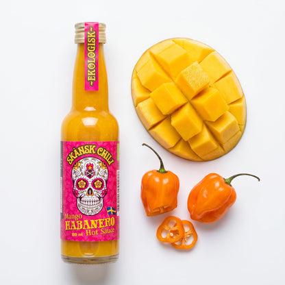 Skånsk Chili Mango Habanero Hotsauce Flasche mit frischen Mangoscheiben und Habanero-Chilis