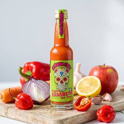 Skånsk Chili Original Habanero Hot Sauce neben ihren Zutaten: rote Habaneros, Zwiebel, Paprika, Knoblauch, Zitrone