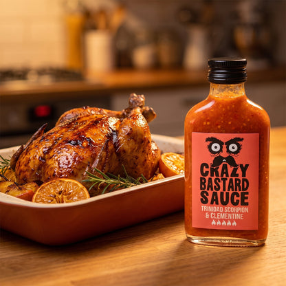 Crazy Bastard Trinidad Scorpion & Clementine Hot Sauce neben glasiertem Brathähnchen mit Orangenscheiben